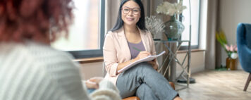 Pleasant psychologist wearing grey trousers smiling to client while speaking with her