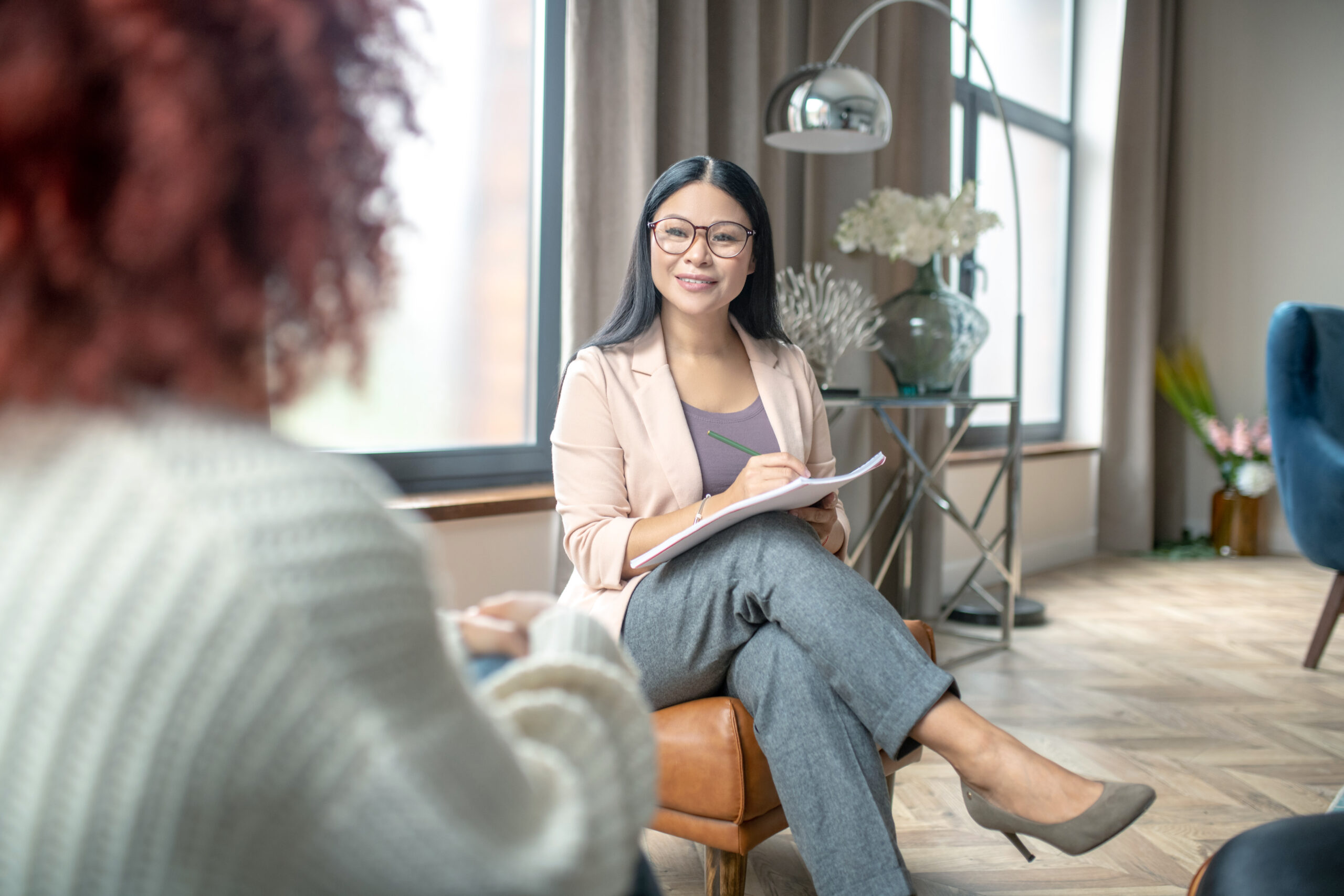 Pleasant psychologist wearing grey trousers smiling to client while speaking with her